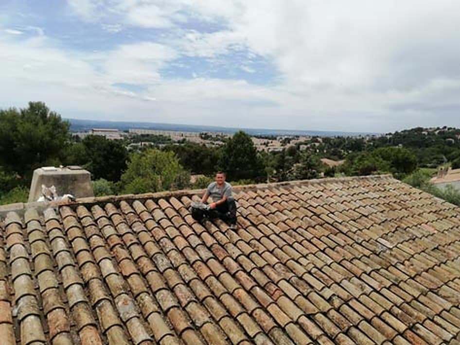 Couvreur au travail sur une toiture en tuiles canal, vue sur le pays d'Aix